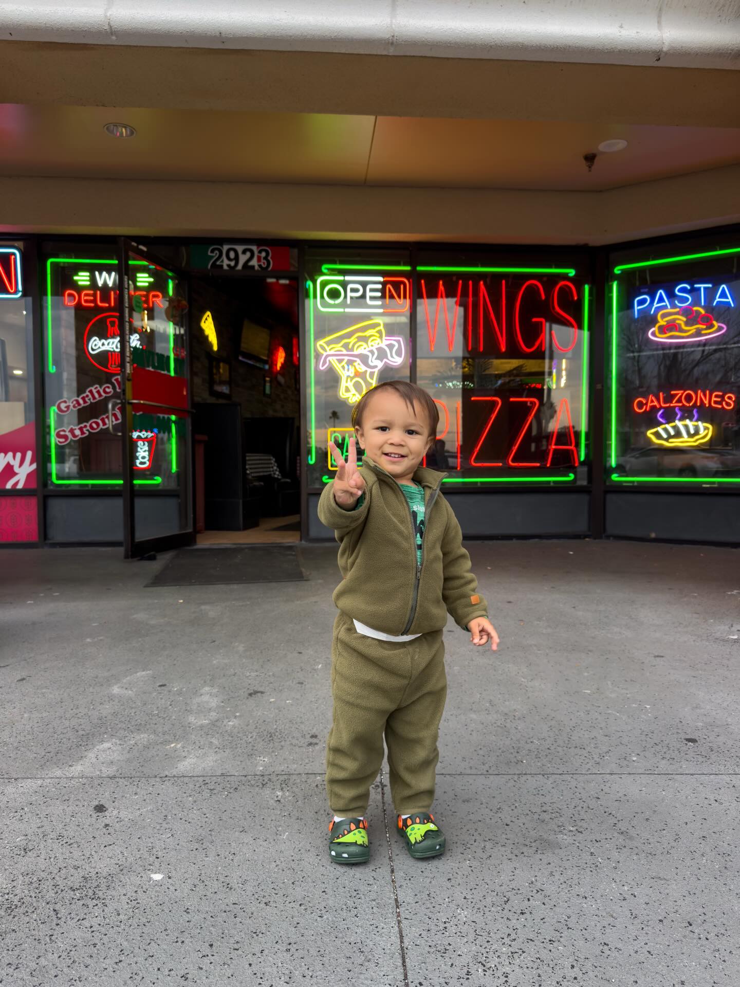 O filho pequeno de Jaque fazendo sinal de paz em frente a uma pizzaria nos Estados Unidos